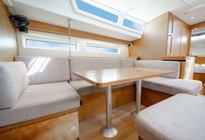 Ein kompakter, gut beleuchteter Innenraum mit einem zentralen Tisch, gepolsterten Sitzgelegenheiten, großen Fenstern und einem Deckenventilator.