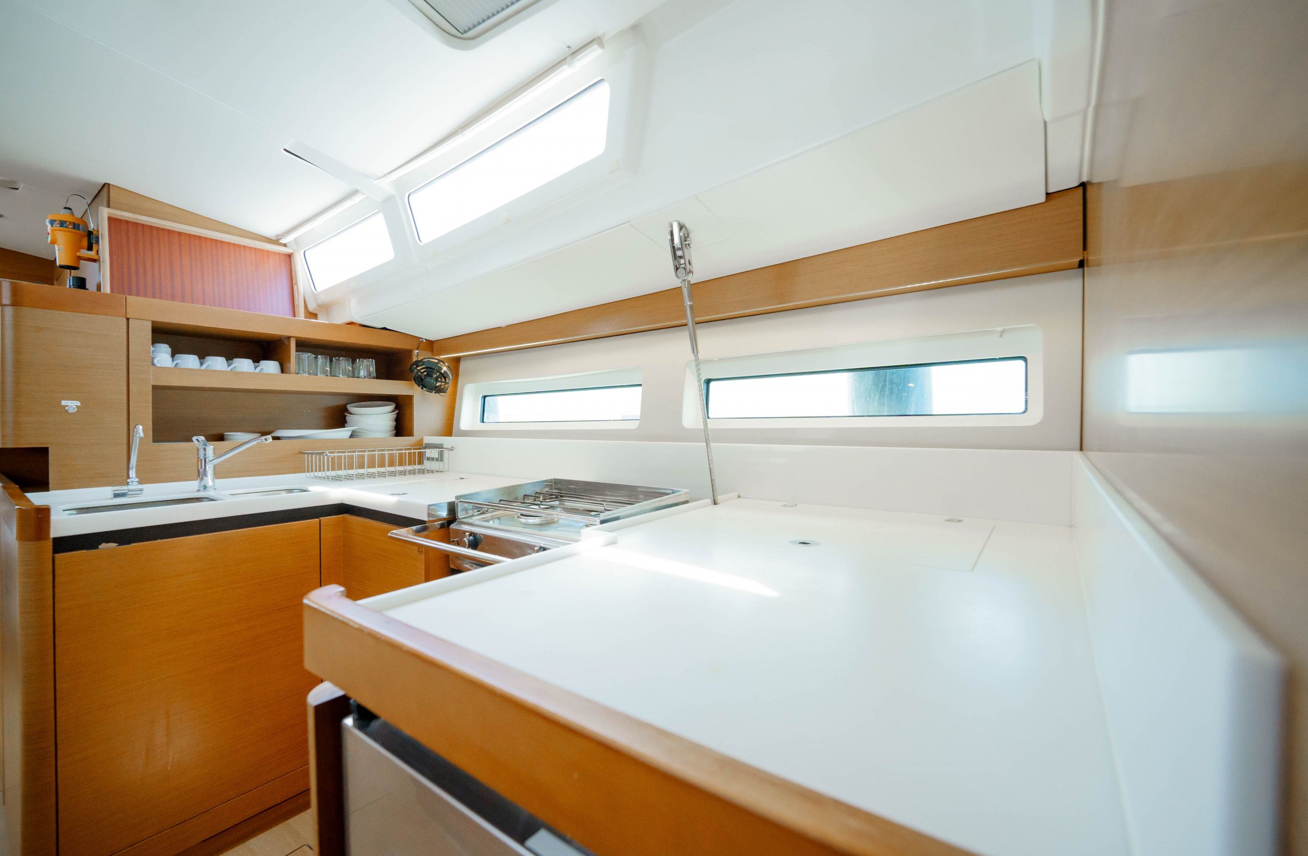 A compact kitchen with a sink, stove, and wooden cabinets. There are windows providing natural light.