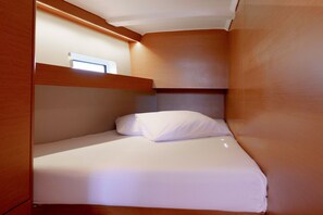 Quarto compacto com uma cama de solteiro, cabeceira de madeira e uma pequena janela.