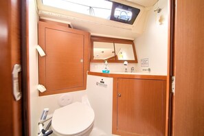 A compact bathroom with a toilet, a sink, a mirror, and a window above the sink. - Sun-Kissed Sailing Adventure in Northern Croatia (Punat)