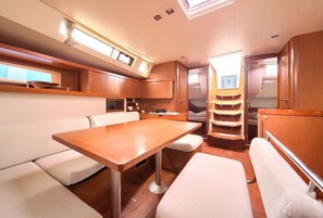 A compact interior with a dining table, cushioned seating, a small kitchenette, and a window for natural light. - Sun-Kissed Sailing Adventure in Northern Croatia (Punat)