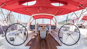 A boat deck with a central steering wheel, two side steering wheels, a wooden floor, and a red canopy. - Sun-Kissed Sailing Adventure in Split, Croatia (Split)