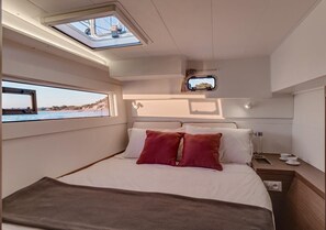 Ein Schlafzimmer mit Bett, Kissen, einem Nachttisch, einem Fenster und einem Dachfenster.