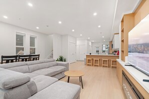 Ein modernes Wohnzimmer mit Ecksofa, rundem Couchtisch und Küchenbereich mit Holzschränken und einer Bar.