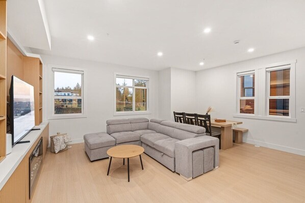 A modern living room with a grey sectional sofa, a round coffee table, and a TV on a wooden stand.