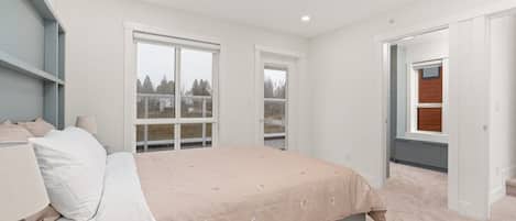 A bedroom with a bed, a nightstand, a window, and a door leading to another room.