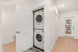 A laundry room with a front-loading washer and dryer, a wooden floor, and a door leading to another room.