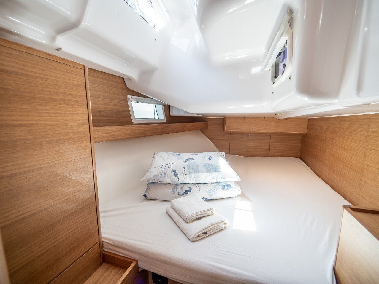 A compact cabin with a single bed, a small window, and a wooden storage compartment.