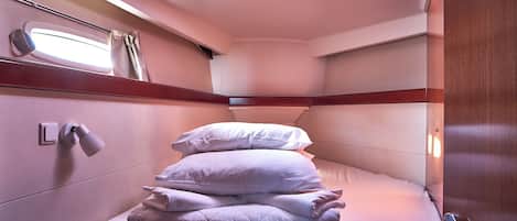 A compact, well-lit cabin with a bunk bed, a window with curtains, and a small bedside table.