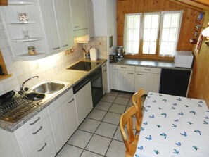 A compact kitchen with a sink, stove, and a dining area with a table. - Giferblick Appartement/Fewo, Dusche oder Bad, WC 3-Bettwohnung by Interhome (Zweisimmen)