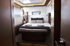 A compact, well-lit bedroom with a bed, bedside tables, a potted plant, and a window. - Sun-Kissed Sailing Adventure in Islas Sarónicas (Alimos)