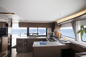 A modern kitchen with a large window, a built-in stove, and a small refrigerator. - Sun-Kissed Sailing Adventure in Islas Sarónicas (Alimos)