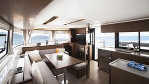 Interni moderni di uno yacht, con zona pranzo, cucina e posti a sedere vicino alle finestre.