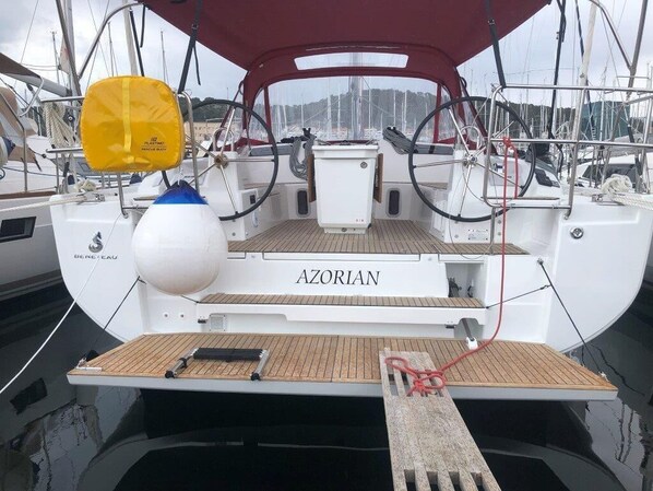 Een boot genaamd AZORIAN afgemeerd in een jachthaven met een houten dek, een reddingsboei en een lier.