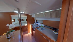 A compact kitchen with a stove, sink, and upper bunk bed. - Dubrovnik Delight: A Sun-Kissed Sailing Experience (Komolac)