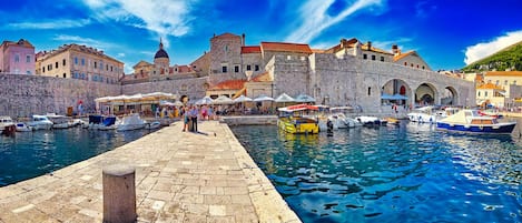 A historic waterfront with stone buildings, a dock with boats, and a paved walkway.