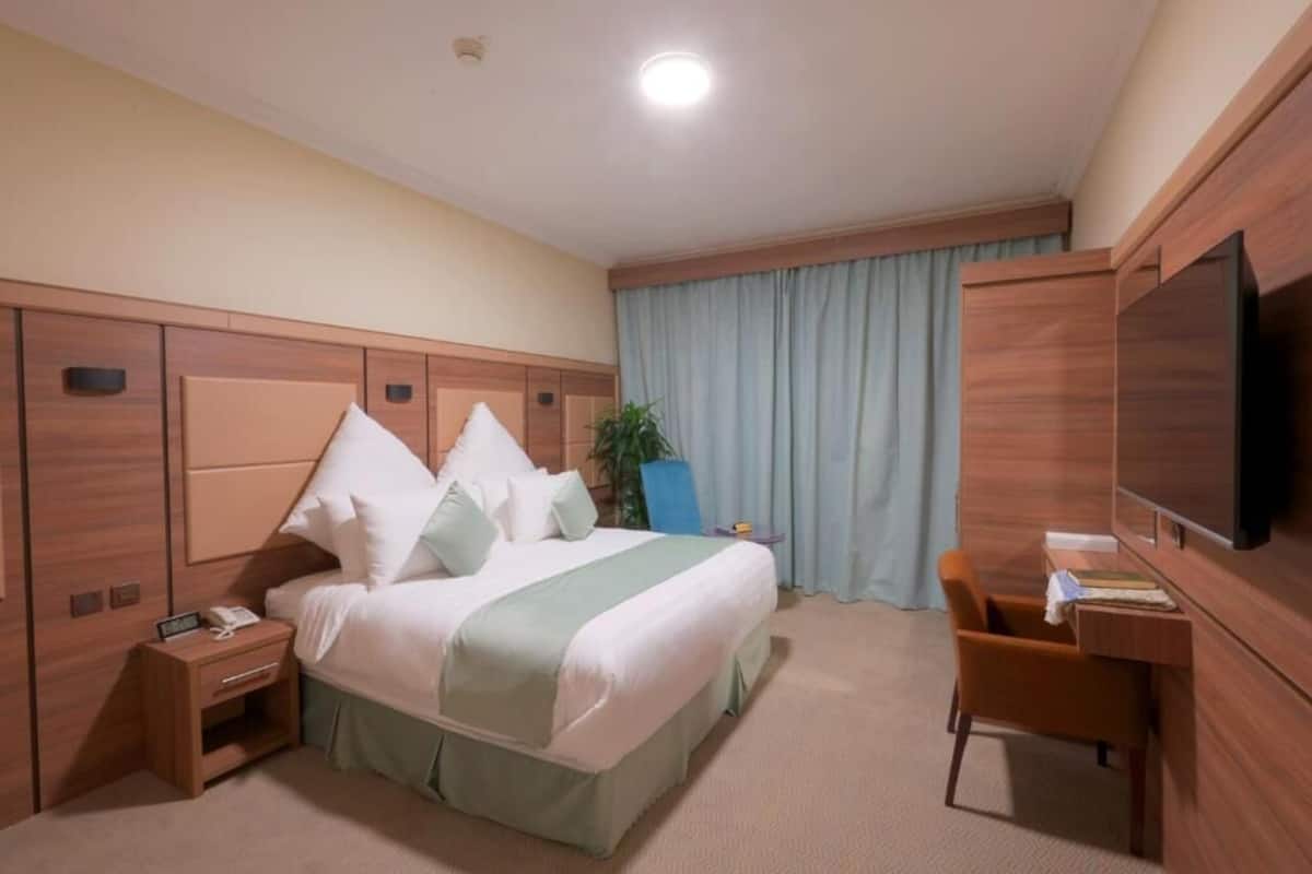 A hotel room with a bed, a desk, a chair, a TV, and a window with curtains.