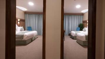 Habitación de hotel con dos camas, un ventanal con cortinas, una mesita de noche y una lámpara de pared.