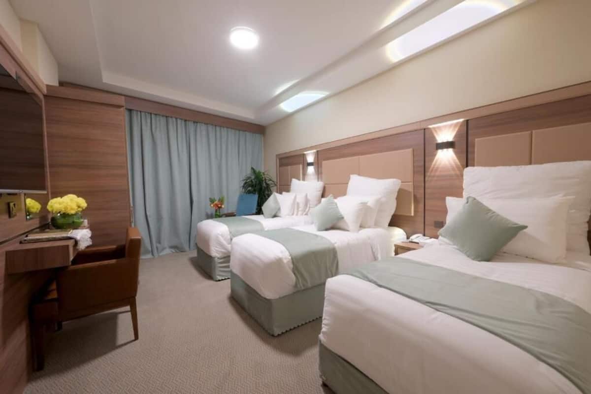 A hotel room with two beds, a desk, a chair, a TV, and a window with curtains.