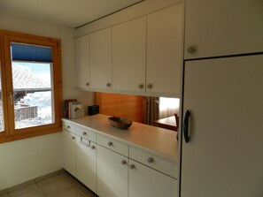 A kitchen with white cabinets, a wooden countertop, and a window with blinds. - Hübeli (Chapman) Appartement/Fewo, Dusche oder Bad, WC, 2 Schlafräume by Interhome (Zweisimmen)