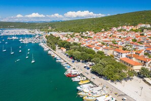 A coastal town with a marina, buildings with red roofs, and a hilly backdrop.