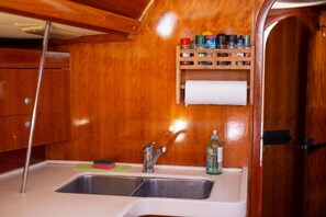 A compact kitchen with a sink, a wooden shelf with various containers, and a paper towel holder. - Sun-Kissed Sailing Adventure in Northern Croatia (Punat)