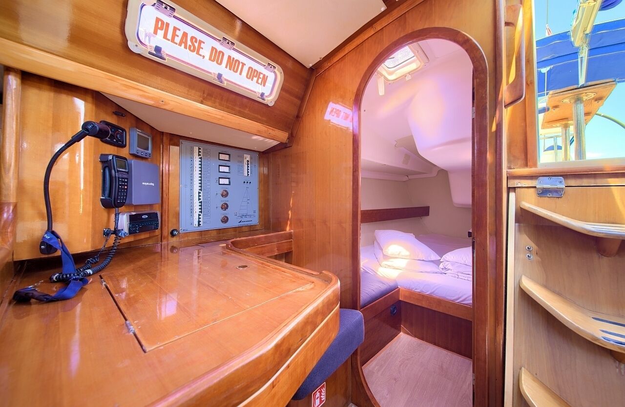 Een compacte hut met een houten inrichting, een bedieningspaneel met diverse knoppen en een telefoon, en een bed met hoofdeinde.