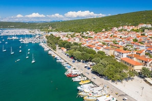 A coastal town with a marina, buildings with red roofs, and a hilly backdrop.