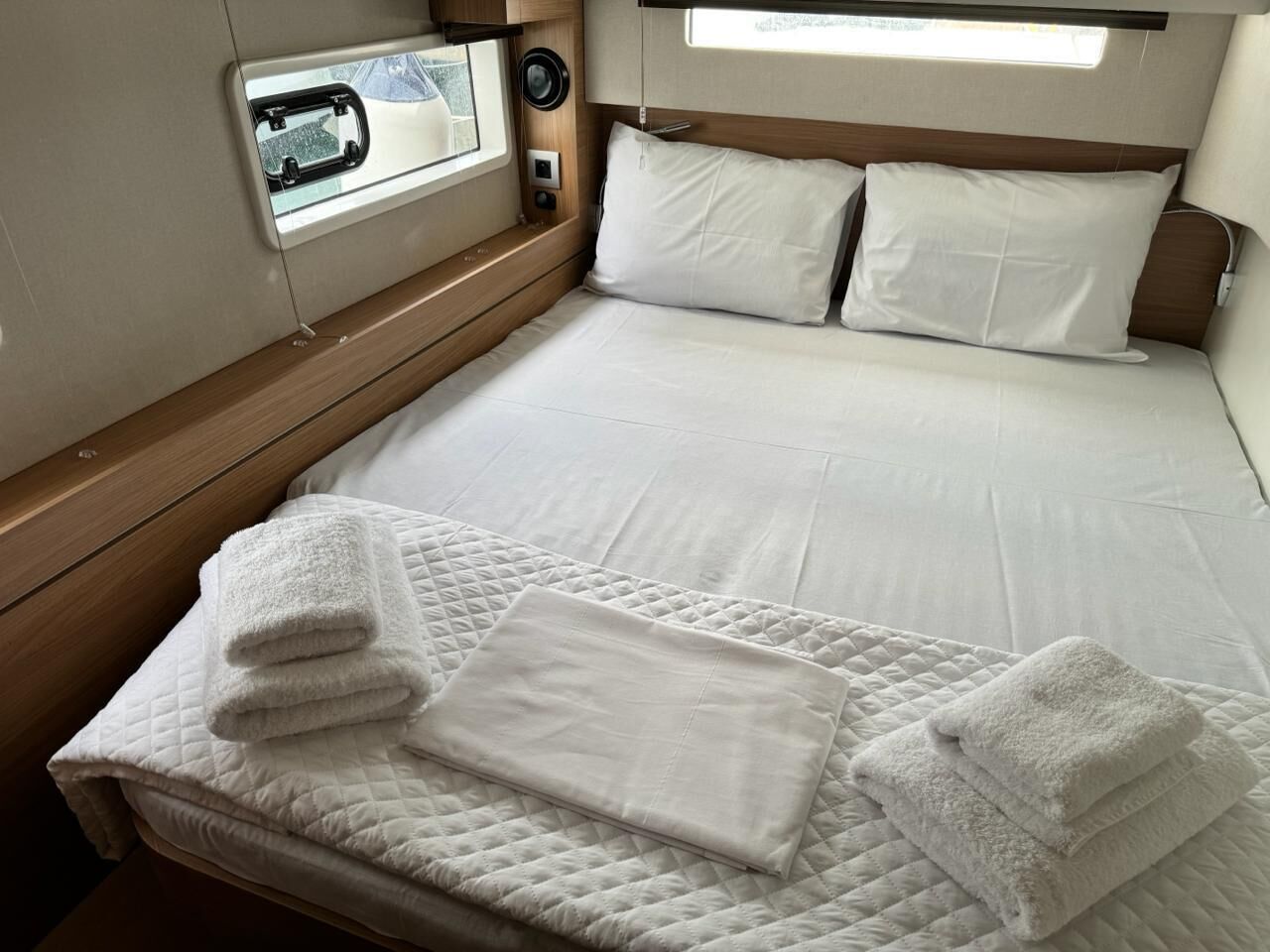 A bed with white linens, a quilted blanket, and folded towels.