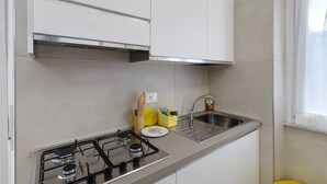 Eine Küche mit Gaskochfeld, Spüle aus Edelstahl und weißen Schränken.