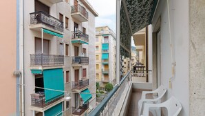 Ein schmaler Balkon mit Blick auf angrenzende Mehrstöckige Gebäude, einem Metallgeländer und zwei weiße Plastikstühle.