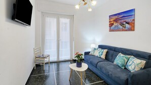Ein Wohnzimmer mit Flachbildfernseher, einer Couch, einem Sessel, einem kleinen Tisch und einem Gemälde.
