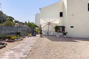 Un patio con un sendero de grava, mobiliario exterior y un paraguas grande.
