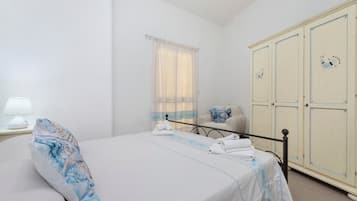 Quarto de hotel com cama, mesa de cabeceira, abajur, janela com cortinas, guarda-roupa e uma cadeira.