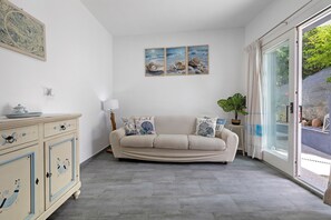 A room with a beige sofa, a cabinet with decorative handles, and a large window with a view of greenery. - Holiday Home 'Casa Campitanesu' with Mountain View, Private Garden and Wi-Fi (Viddalba)