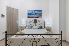 A bedroom with a bed, two bedside tables, a nightstand, a door, and a wall-mounted picture. - Holiday Home 'Casa Campitanesu' with Mountain View, Private Garden and Wi-Fi (Viddalba)