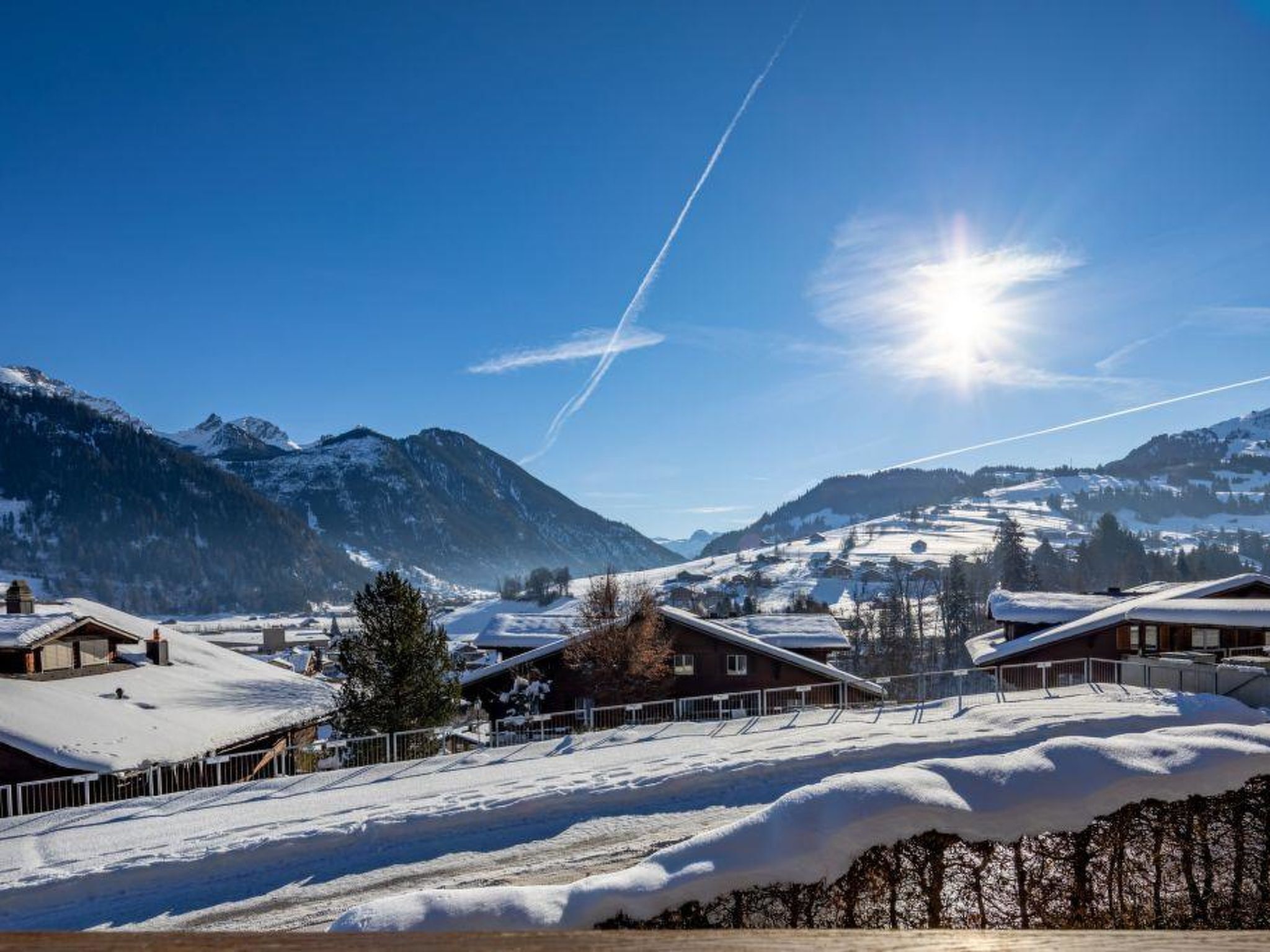 A snow-covered mountain village with houses, a clear sky, and a bright sun.
