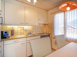 A compact kitchen with white cabinets, a built-in oven, and a window with sheer curtains. - Hübeli (Moosmatten) Appartement/Fewo, Dusche oder Bad, WC, 1 Schlafraum by Interhome (Zweisimmen)