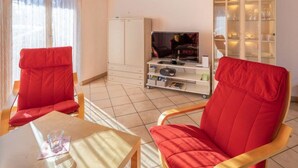 A living room with two red chairs, a television, a cabinet, and a glass cabinet with shelves. - Hübeli (Moosmatten) Appartement/Fewo, Dusche oder Bad, WC, 1 Schlafraum by Interhome (Zweisimmen)