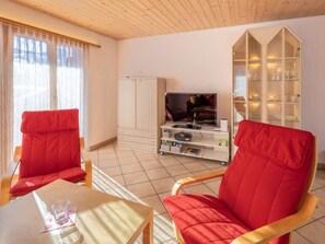 A living room with two red chairs, a television, a cabinet, and a glass cabinet with shelves. - Hübeli (Moosmatten) Appartement/Fewo, Dusche oder Bad, WC, 1 Schlafraum by Interhome (Zweisimmen)