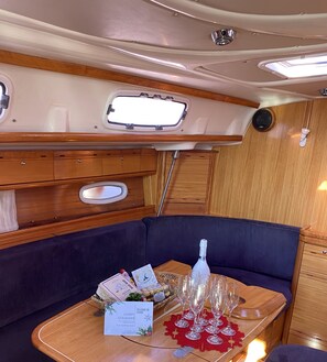 A cozy RV interior with a dining area, a small table with a bottle, glasses, and a welcome card. - Sun-Kissed Sailing Adventure in Islas Sarónicas (Alimos)