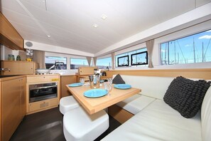 A compact galley with a wooden table, white seating, and a large window with a view of sailboats. - Sun-Kissed Sailing Adventure in Northern Croatia (Punat)