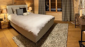 Une chambre à coucher avec un grand lit, des murs en bois, une table de chevet avec une lampe, une commode et une fenêtre avec des rideaux.