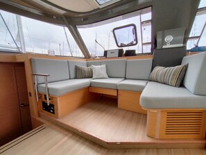 A boat interior with a curved seating area, a small table, and a window with a view of the water. - Sun-Kissed Sailing Adventure in Northern Croatia (Punat)
