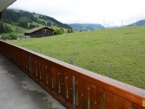 Une clôture en bois surplombe un champ verdoyant, avec un bâtiment visible au loin.