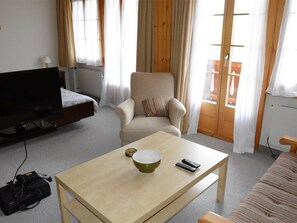 A room with a television, a sofa, a chair, a table with a bowl and remote, and a window with curtains. - Mireille Nr. 4 Appartement/Fewo, Dusche oder Bad, WC 4-Bettwohnung by Interhome (Gstaad)