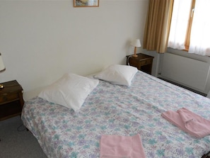 A double bed with floral bedding, two pillows, a nightstand with a lamp, and a window with curtains. - Mireille Nr. 4 Appartement/Fewo, Dusche oder Bad, WC 4-Bettwohnung by Interhome (Gstaad)