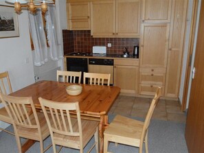A compact kitchen with wooden cabinets, a dining table with chairs, and a dishwasher. - Mireille Nr. 4 Appartement/Fewo, Dusche oder Bad, WC 4-Bettwohnung by Interhome (Gstaad)