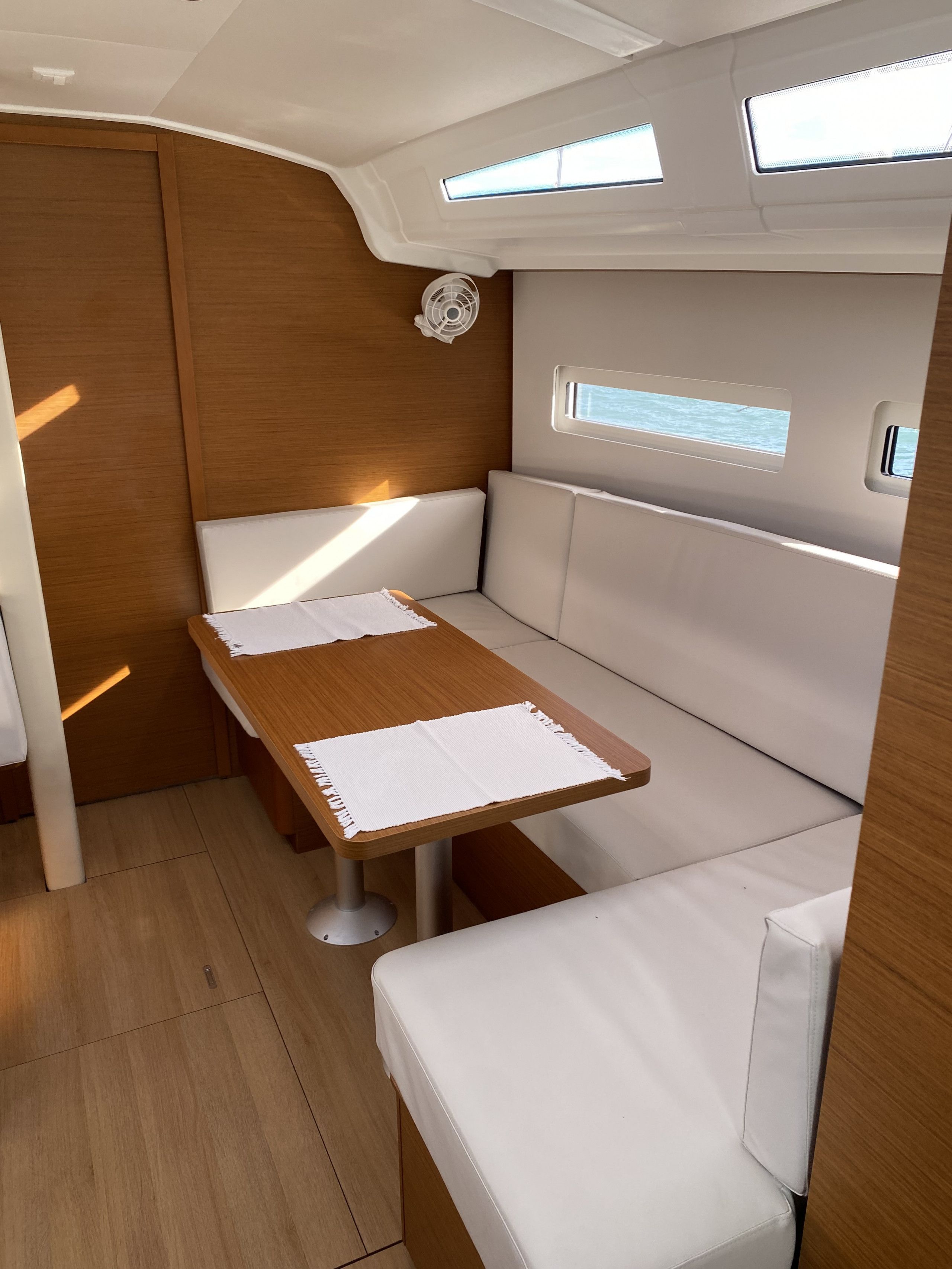 A compact interior with a wooden table, white cushioned seating, and a ceiling fan.