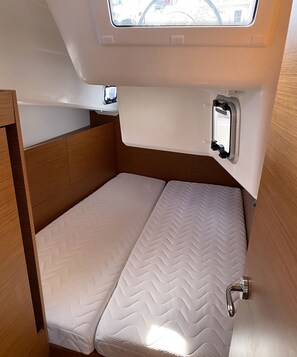 A compact, single-bed RV interior with a wooden headboard, a small window, and a built-in storage compartment.